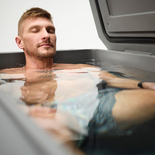 A man soaking in a gray Grizzly 450 cold plunge. His eyes are closed, and he looks at peace; very relaxed. The man has water up to his neck for a deep soak.