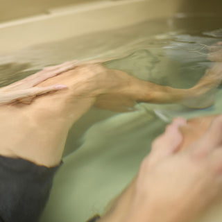 There is a man's legs and hands submerged in water. You can see that they are inside a tan Grizzly 450 cold plunge tub.