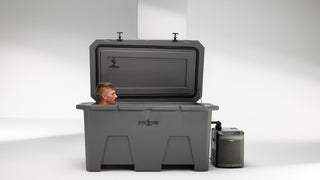 A man using a gray cold plunge tub with his eyes closed, calmly experiencing a deep soak. The cold plunge is sitting indoors in a plain white room. The lid is open as the man is inside. You can see the Desert Plunge logo on the lid and front of the ice bath. The chiller equipment with digital display is hooked up next to the cold plunge.