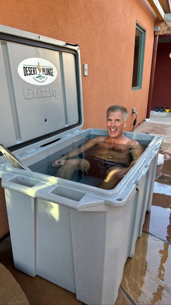 A photo of man enjoying his cold plunge tub outside.