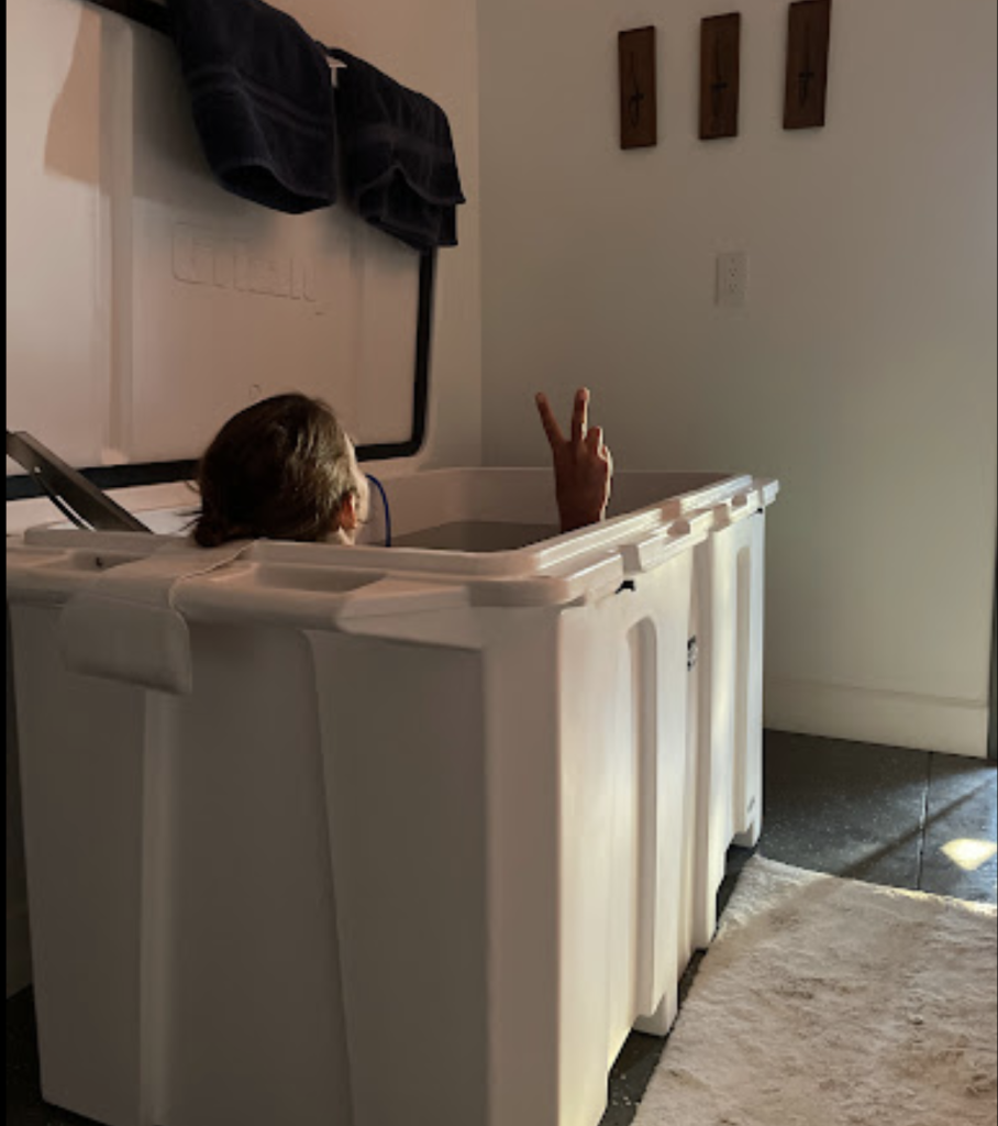 A photo of a woman enjoying her 1/4 horsepower cold plunge tub from Desert Plunge inside her home. She is flashing a peace sign.