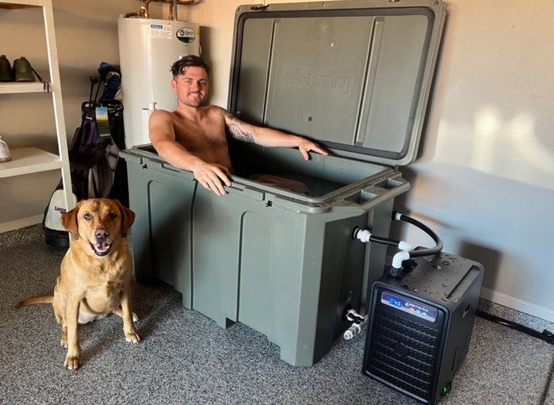 A photo of a man enjoying his 1/4 horsepower cold plunge tub from Desert Plunge inside his home; his cute dog is also in the photo.