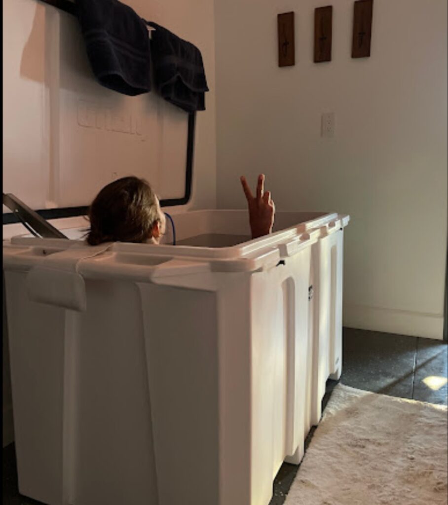 A woman enjoying her 1/4 horsepower cold plunge tub from Desert Plunge inside her home. She is flashing a peace sign.